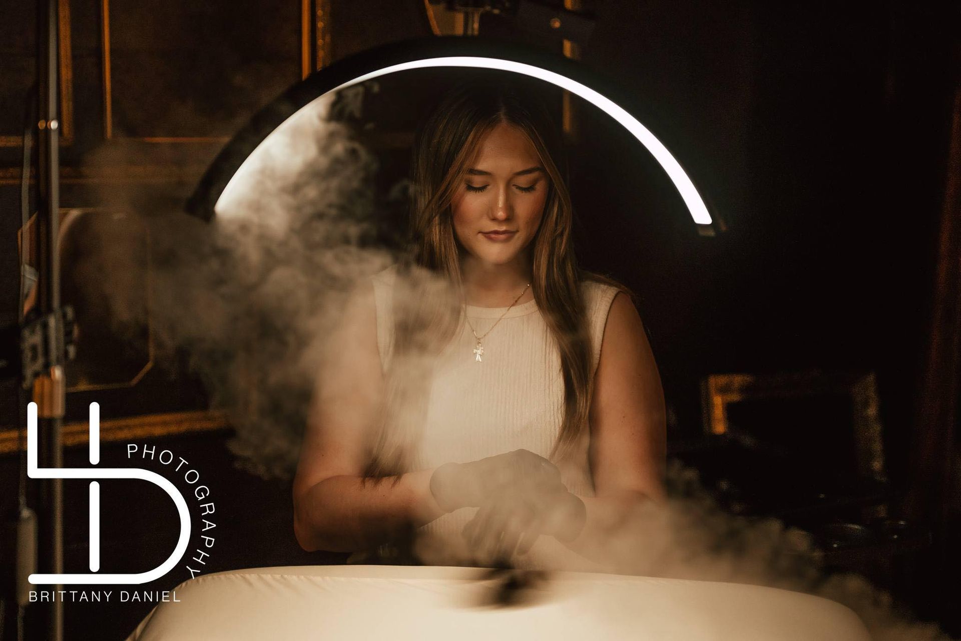 A woman in a white dress is standing under a light with smoke coming out of it.