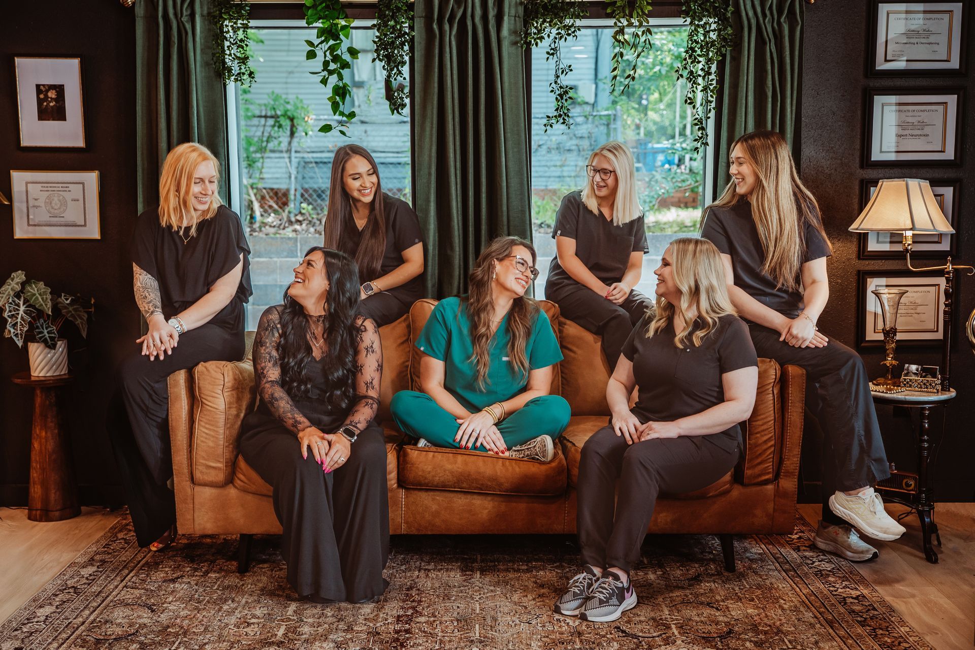 Group of smiling women posing on a brown couch in a room with dark walls.