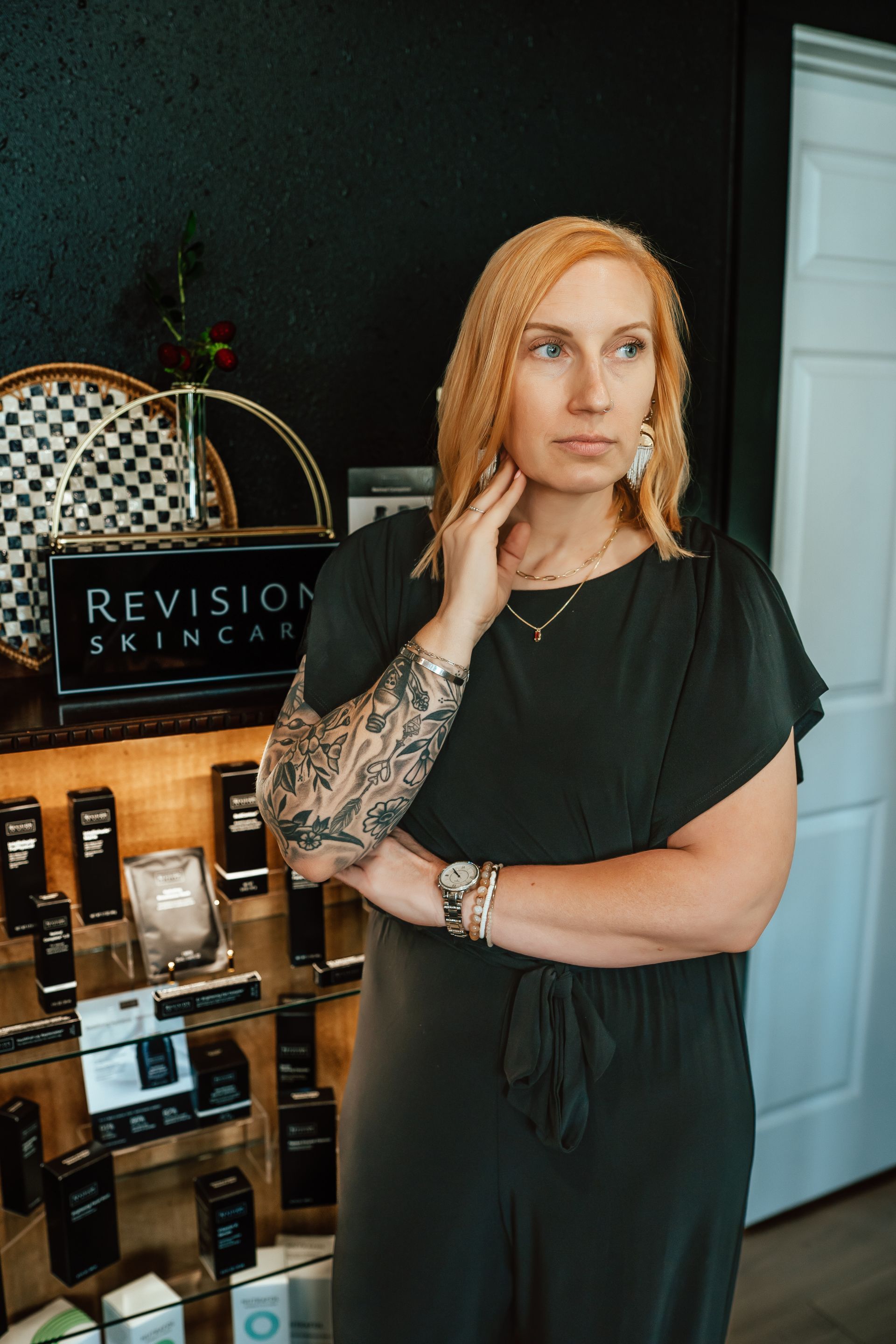 Woman with blonde hair and arm tattoo in front of a display of Revision Skincare products.