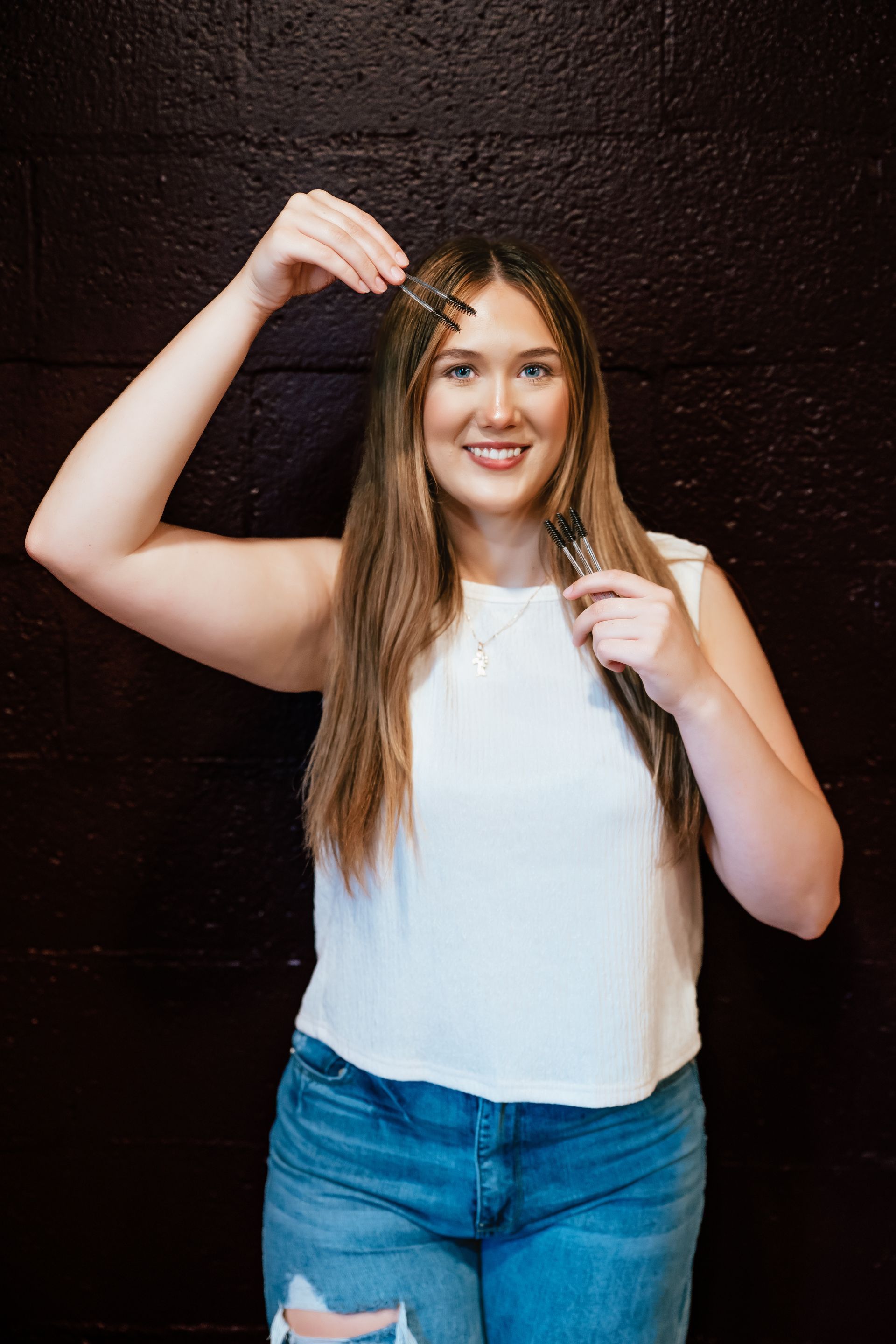 Woman with long brown hair holds key near head; smiles in front of dark wall.
