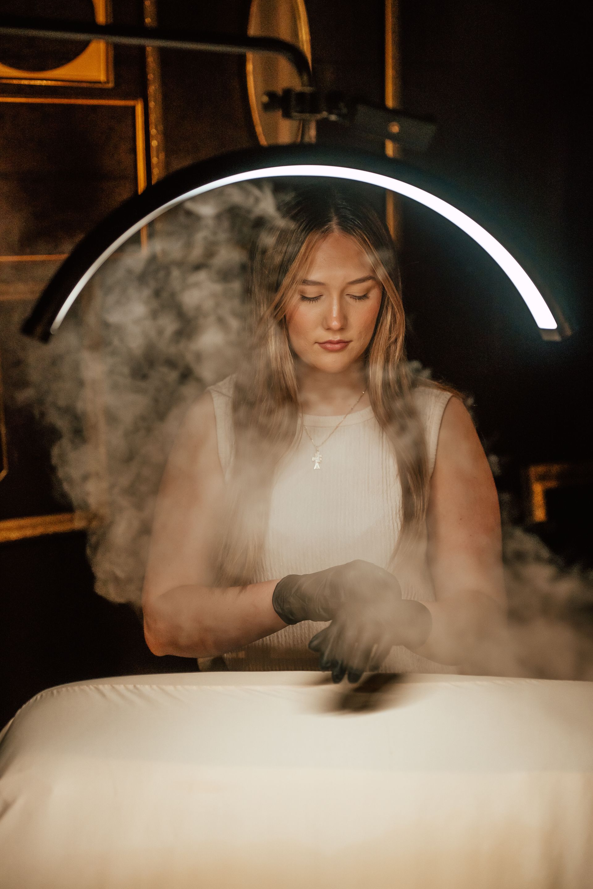 Woman in white dress and gloves surrounded by mist, under a curved bright light.