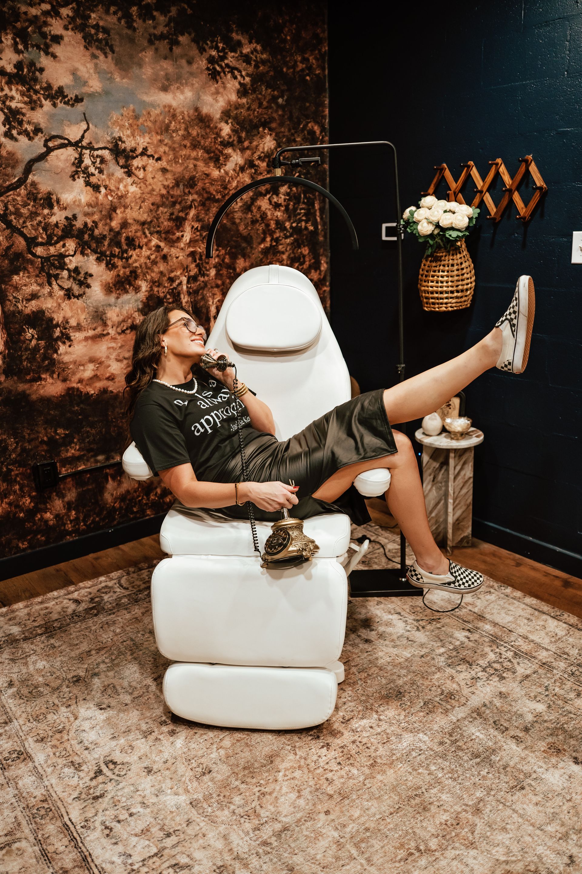 Woman reclining in white chair, legs up, in a stylish room with floral wallpaper, flowers, and patterned rug.