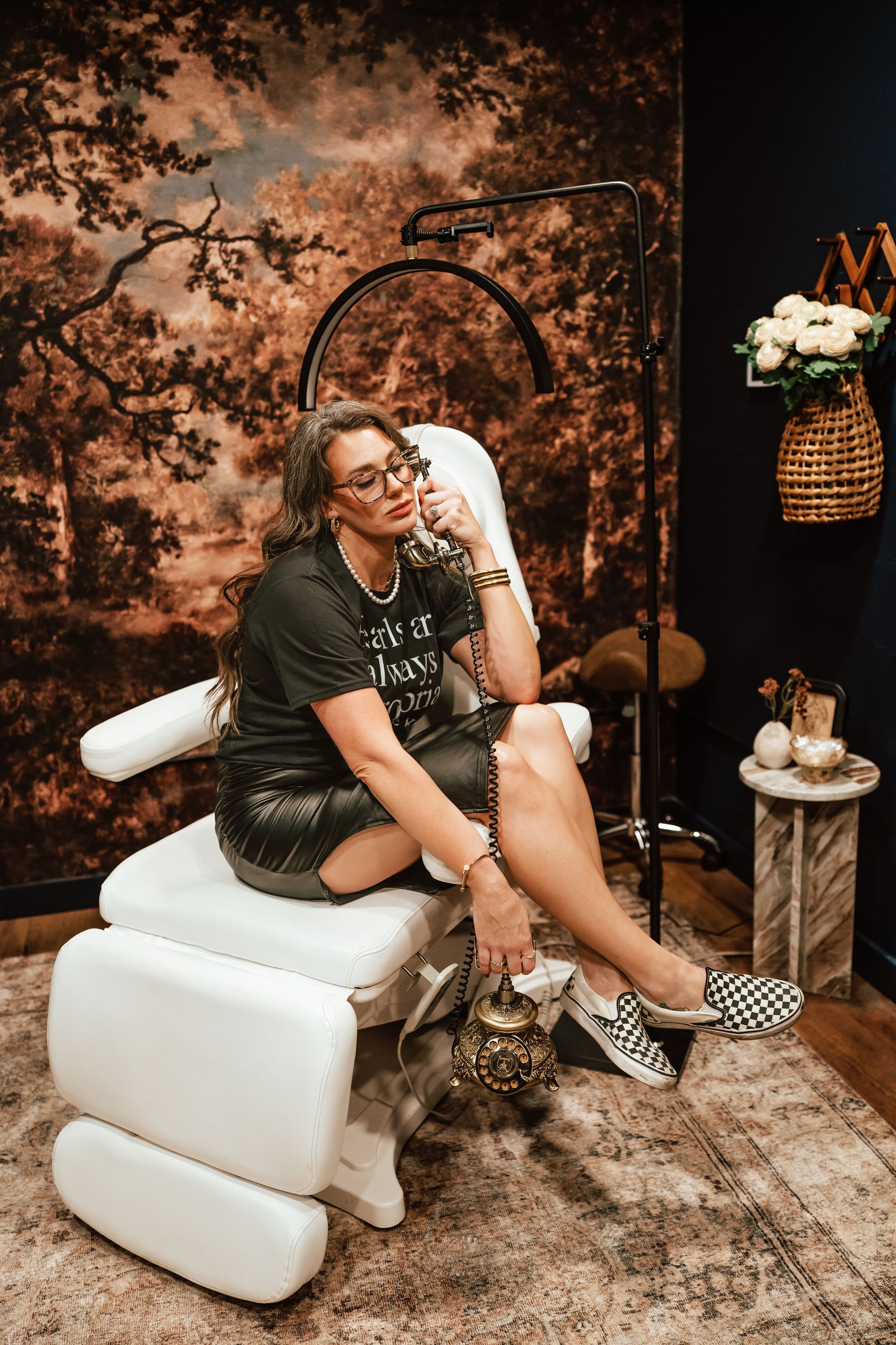 Woman in sparkly skirt sits on medical chair; holding ornate bag.