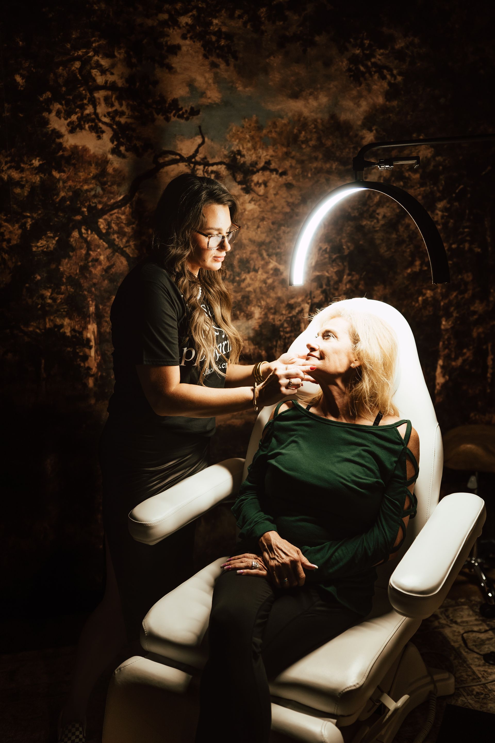 A woman getting a cosmetic procedure with another woman; in a salon.