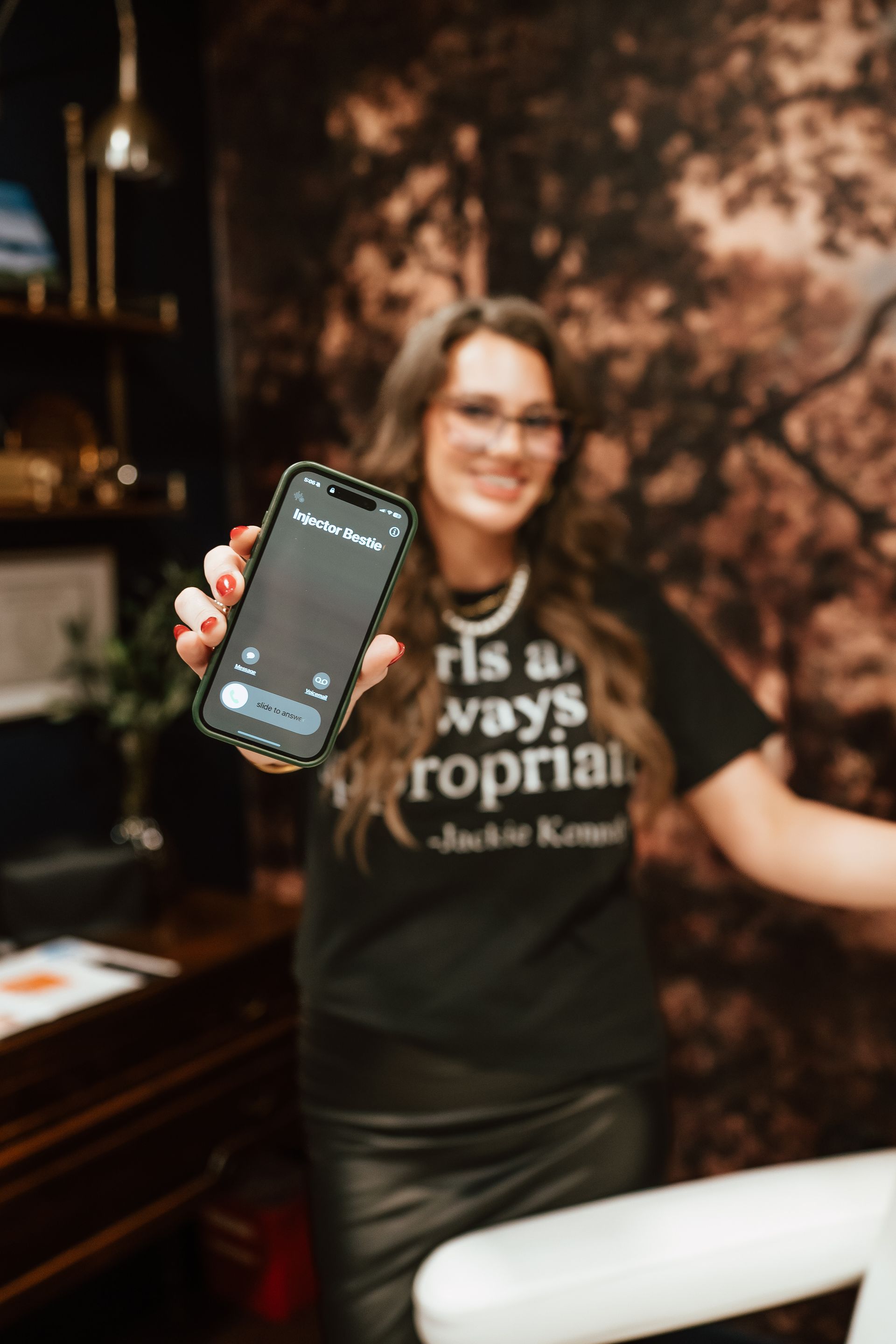Woman in black shirt and leather skirt holds up phone with incoming call; office setting.