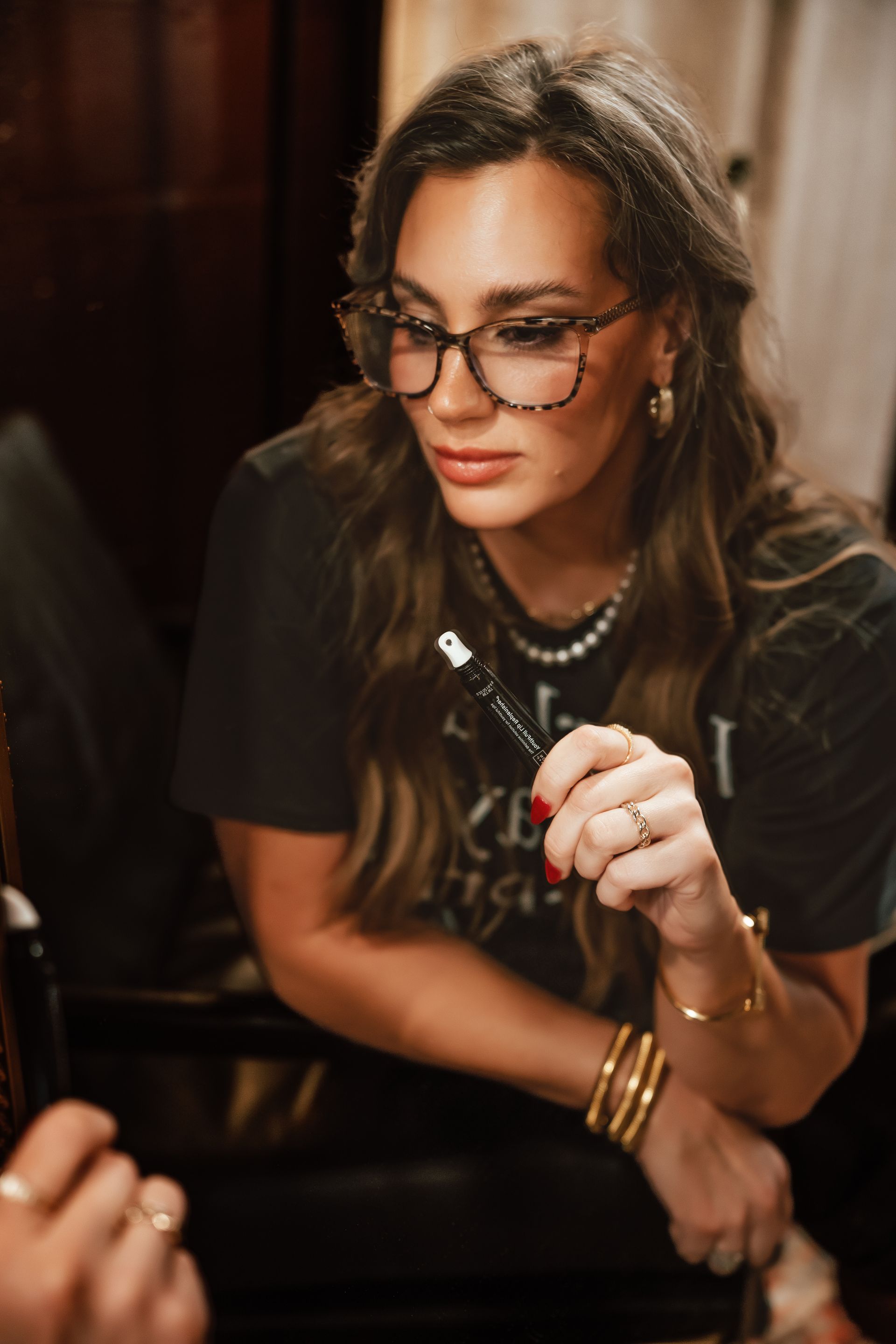Woman in glasses, black t-shirt, jewelry, holding a pen, focused expression.