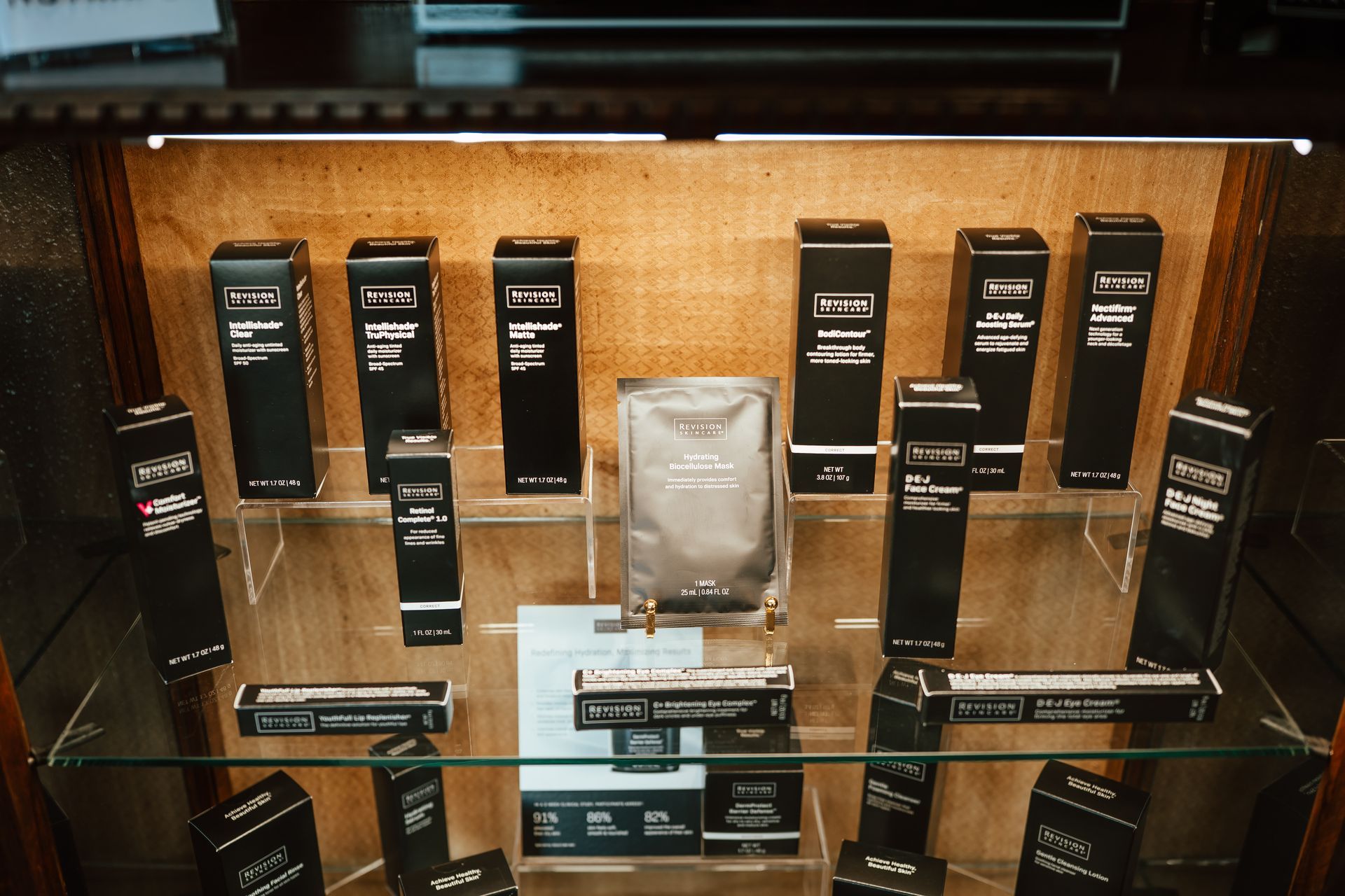 Display case with various black and silver skincare products, organized on clear shelves against a corkboard backdrop.