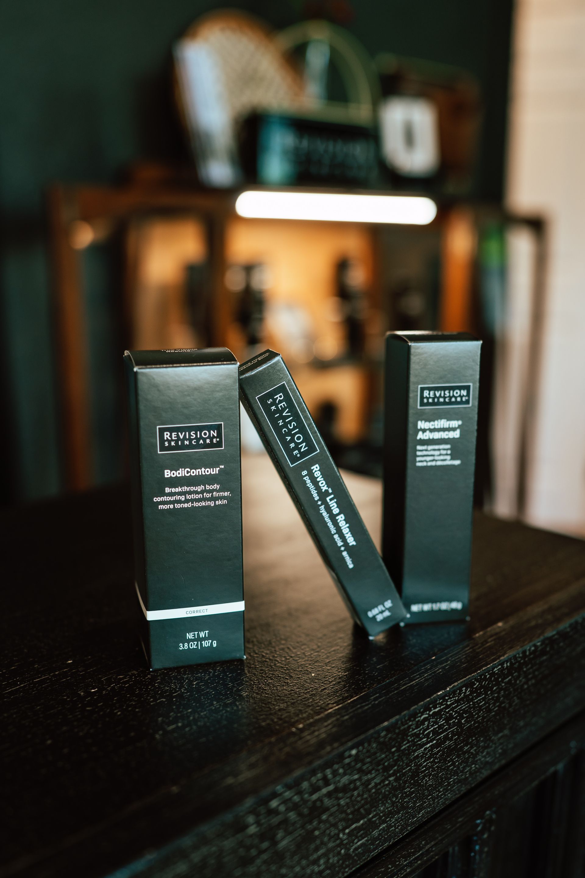 Three black cosmetic product boxes on a dark wooden surface.