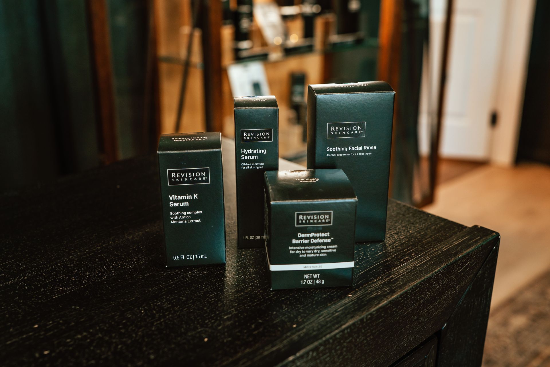 Four black skincare product boxes on a dark table. The boxes are labeled with white text.