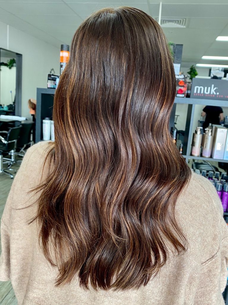 A woman with long brown hair is sitting in a salon - Hairdresser in Mackay, QLD