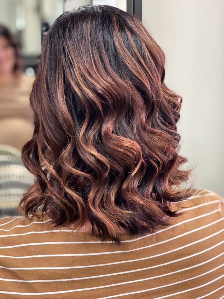 A woman is sitting in front of a mirror with her hair in a striped shirt - Hairdresser in Mackay, QLD
