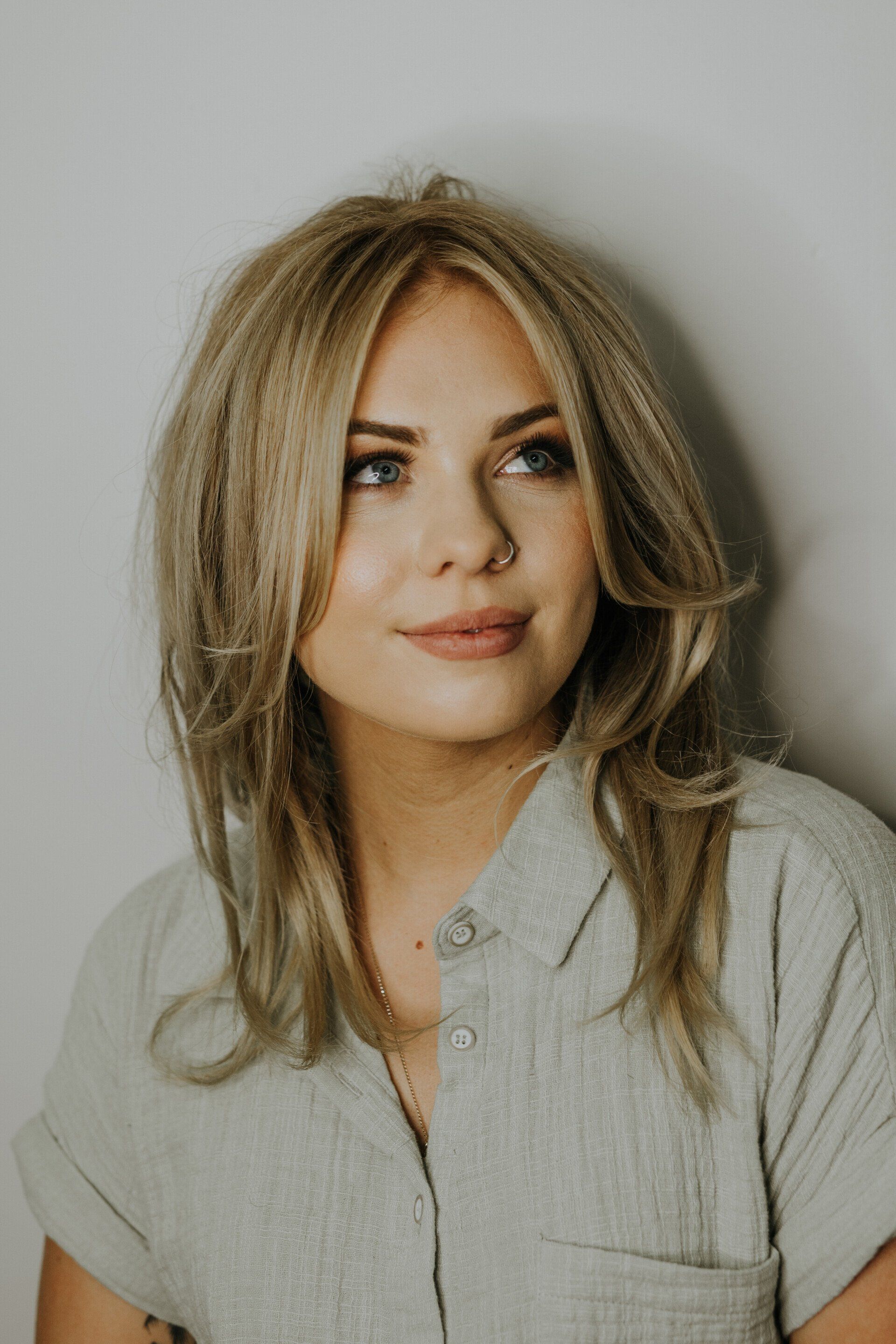 A woman with blonde hair and blue eyes is standing in front of a white wall - Hairdresser in Mackay, QLD