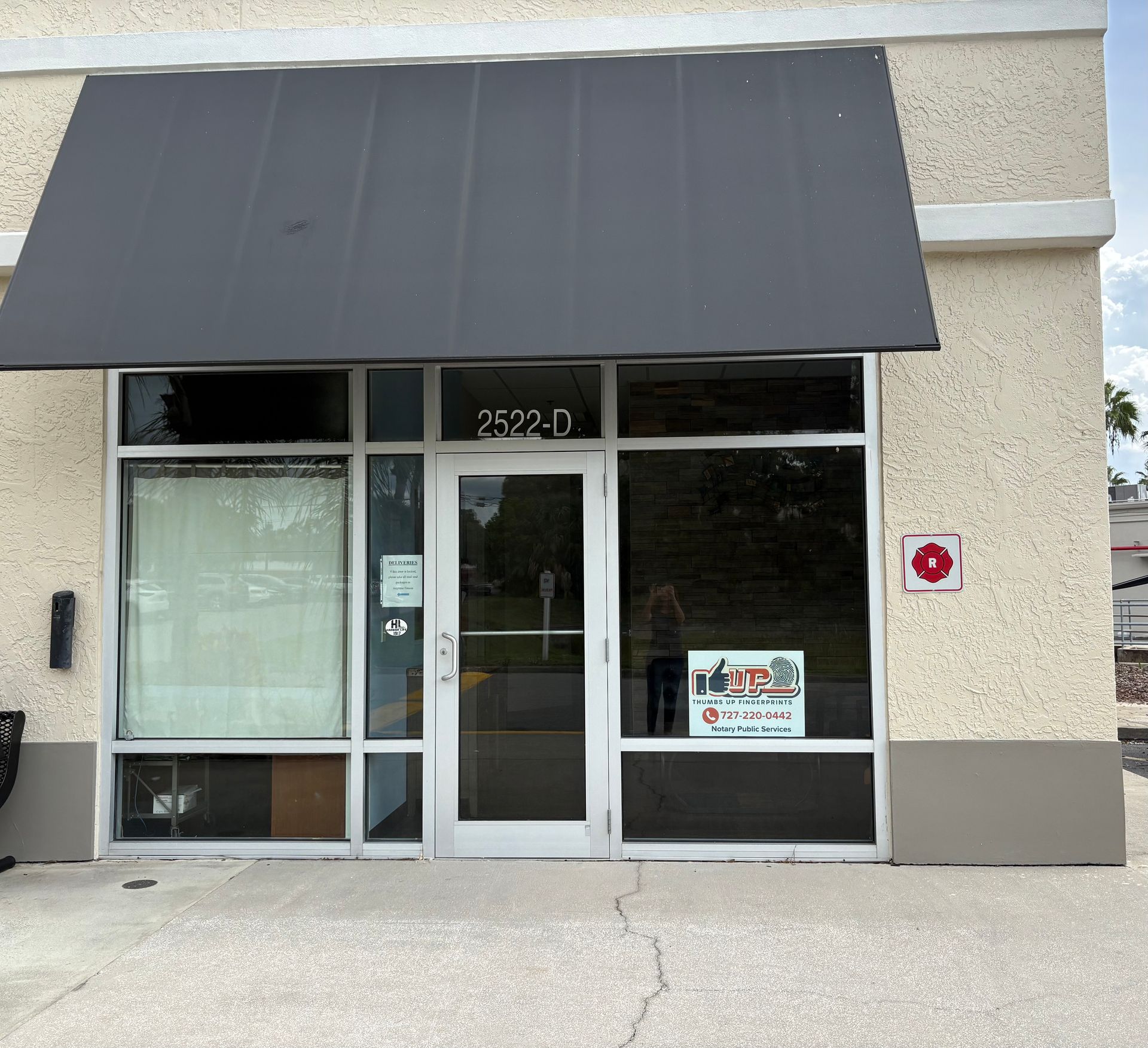 Exterior storefront with dark awning and glass door, address 2522-D. Beige building, sign in window.