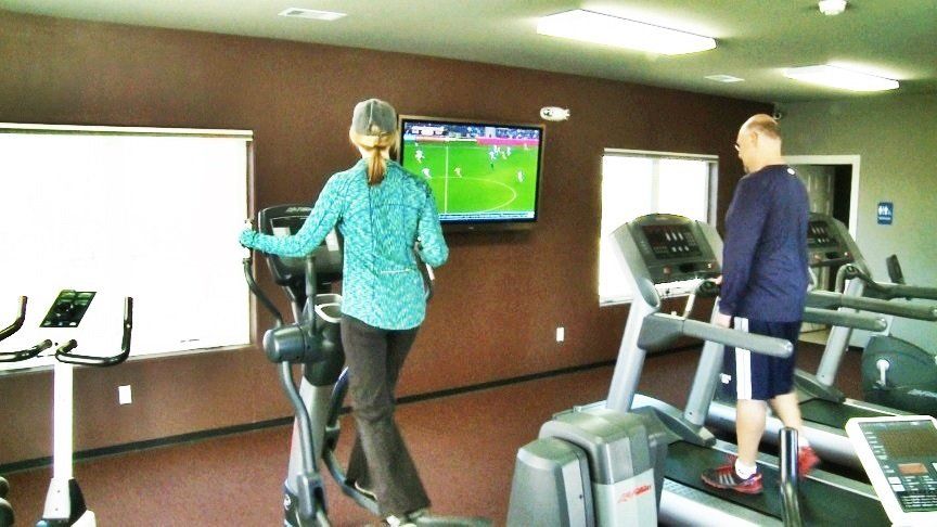 A woman is riding an elliptical in a gym while a man is running on a treadmill