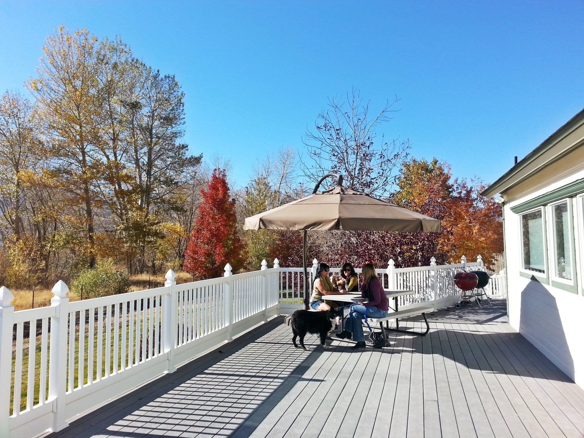A group of people are sitting at a table under an umbrella on a deck.