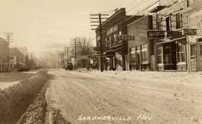 A black and white photo of a snowy street in a small town.