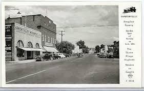 A black and white photo of a city street with cars parked on the side of the road.