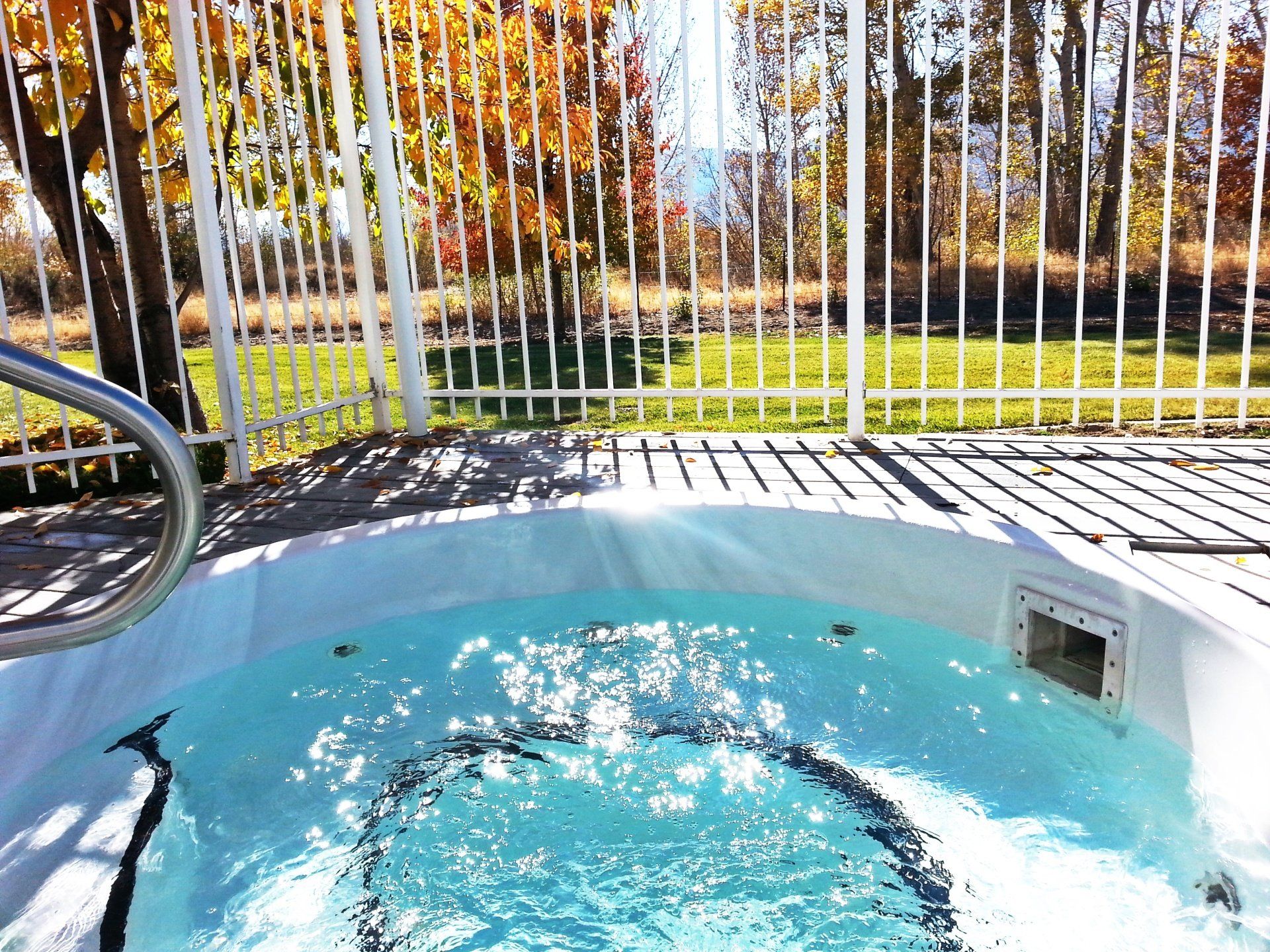 A hot tub is sitting on a deck next to a fence.