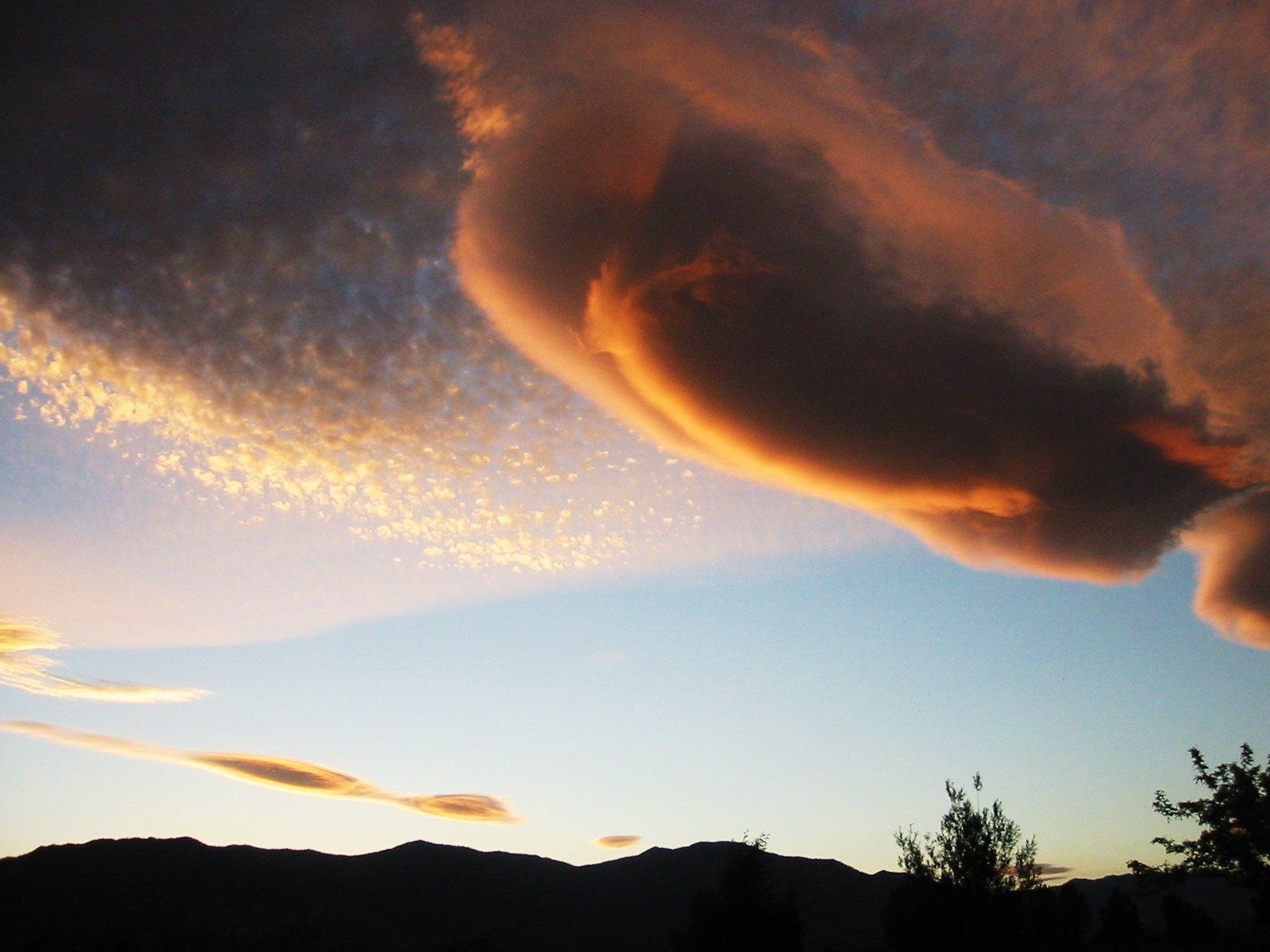 A cloudy sky with a few trees in the foreground