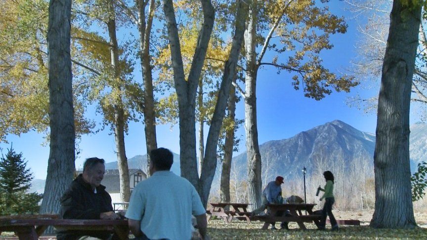People sitting at picnic tables in a park with mountains in the background