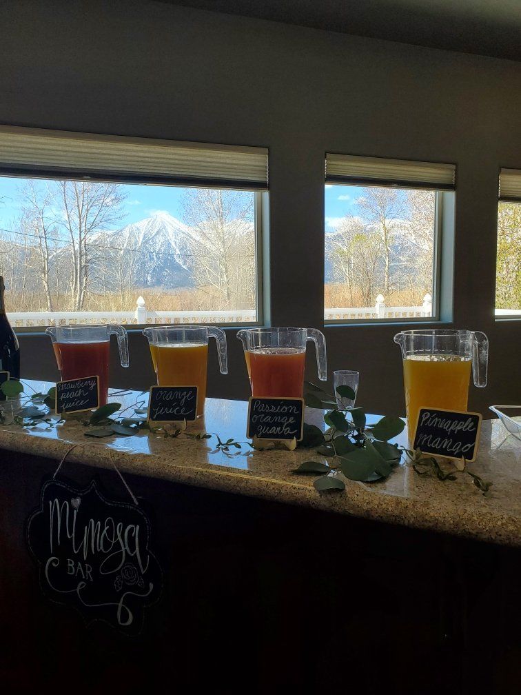 Three pitchers of juice are lined up on a counter in front of a window.