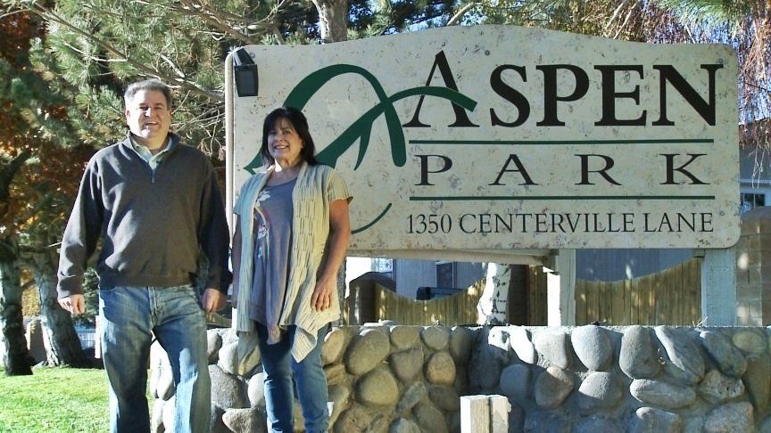 A man and a woman standing in front of a sign for aspen park