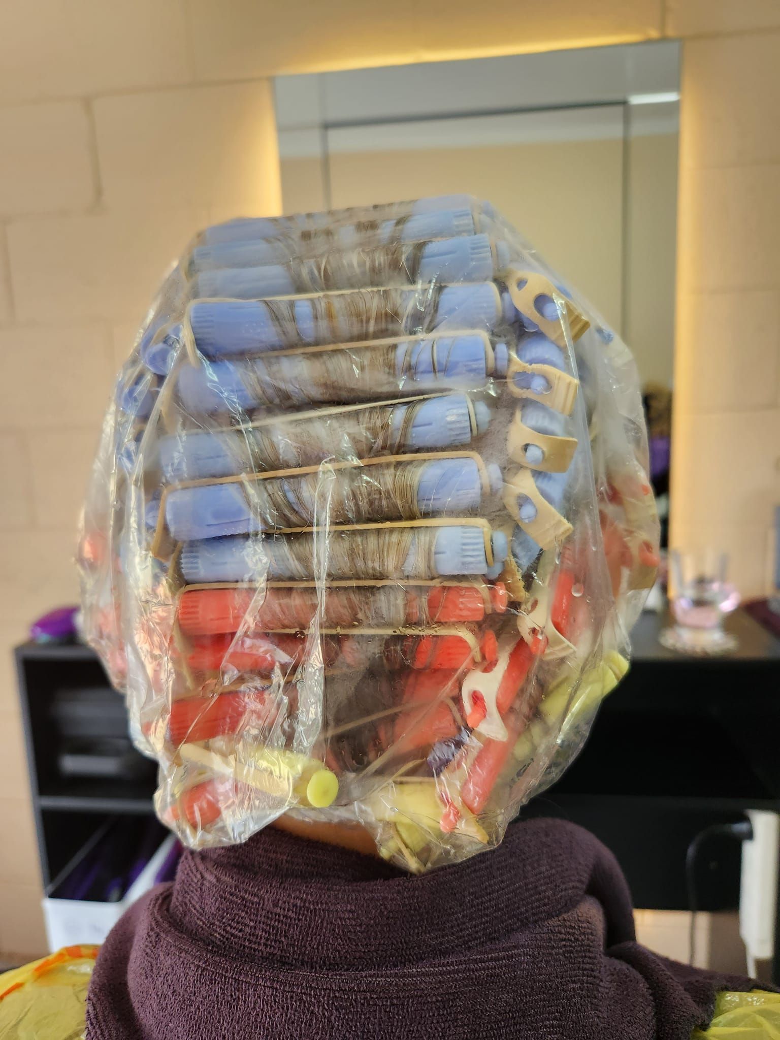 Person with hair rollers under a plastic cap in a salon, wrapped in a towel. — Amore 'D' Hair Studio in Mudjimba, QLD