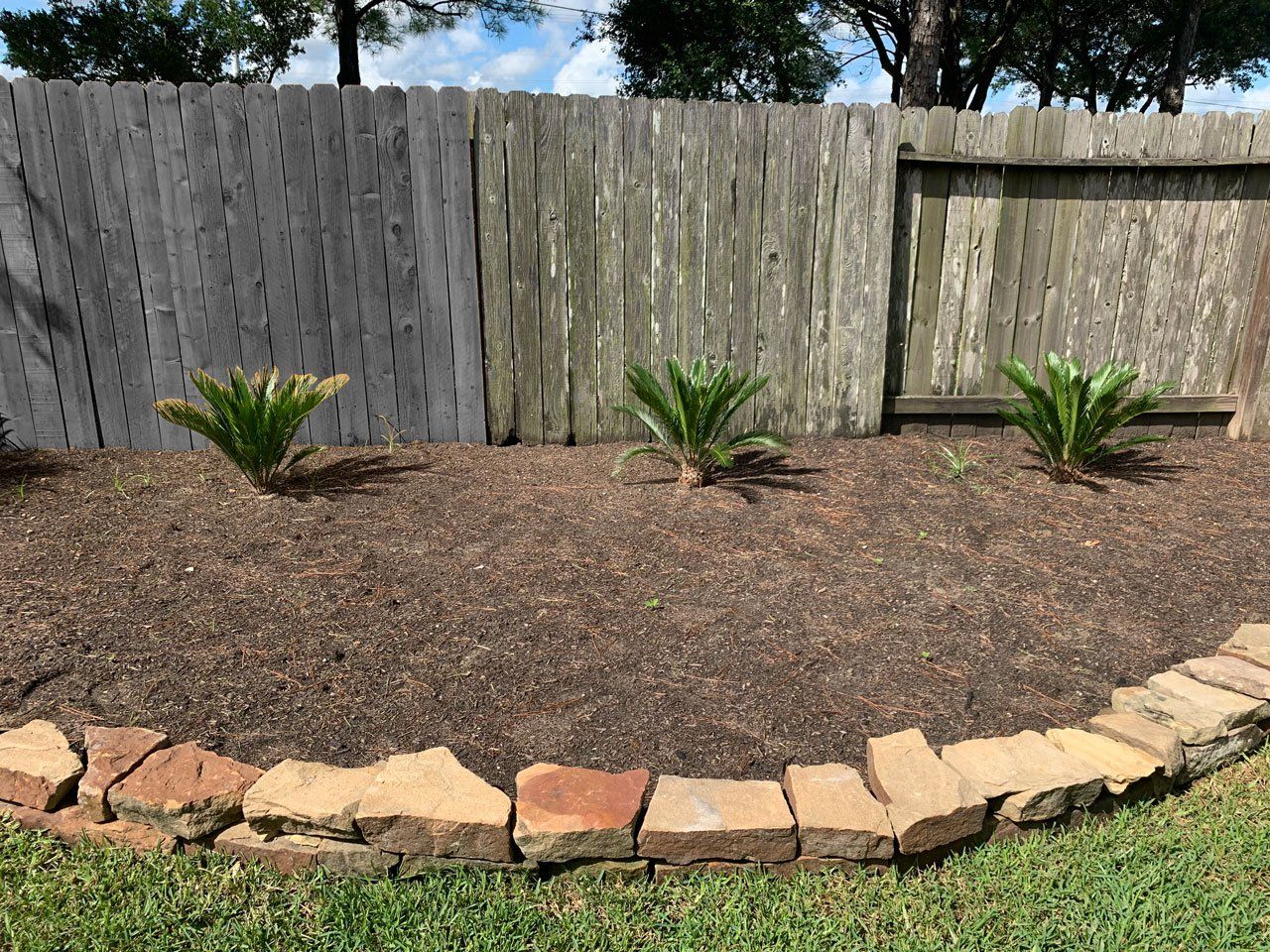 A wooden fence is behind a stone border in a yard.