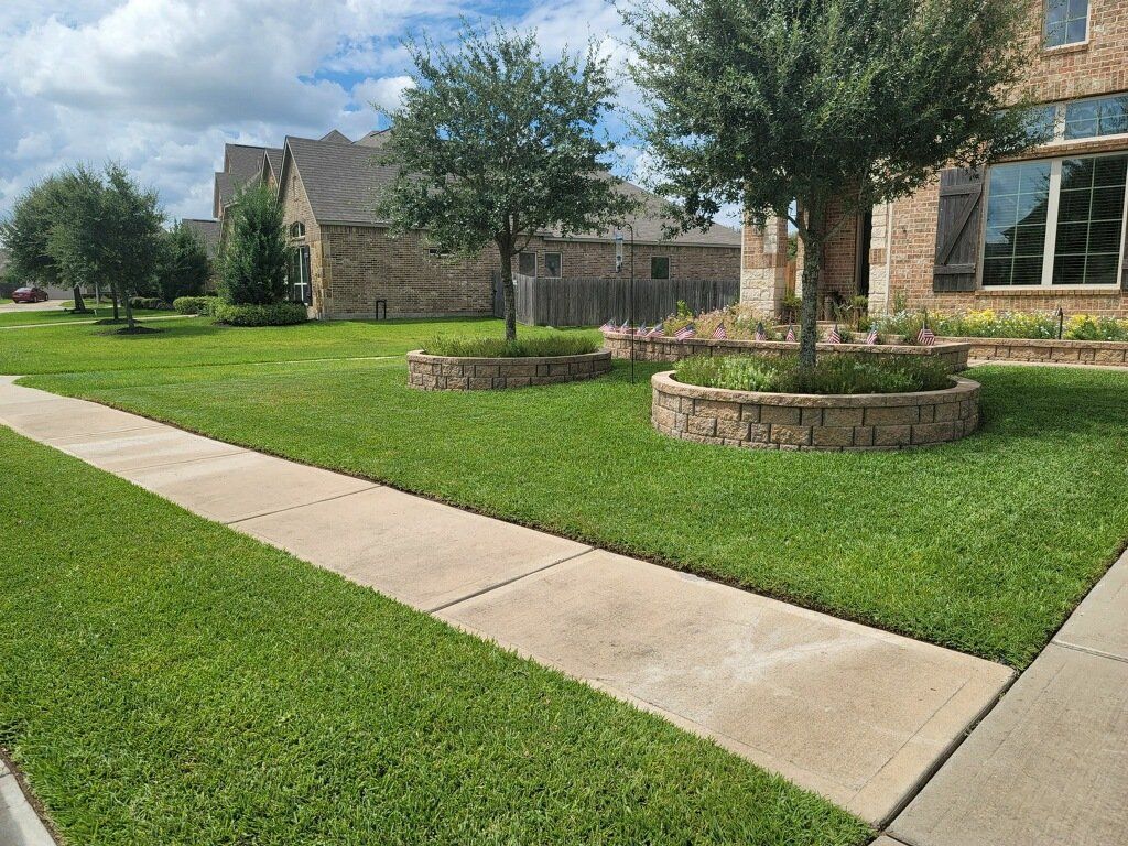 A lush green lawn with a sidewalk and trees in front of a house.