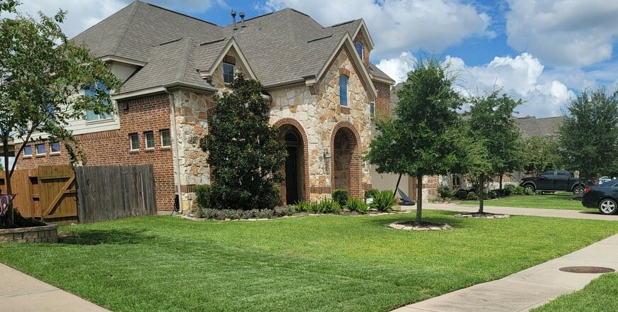 A large brick house with a lush green lawn and a car parked in front of it.