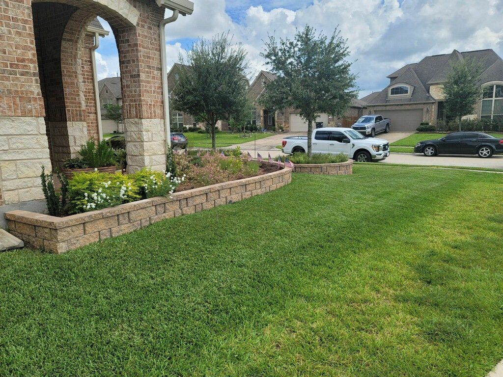A lush green lawn in front of a brick house with cars parked in front of it.