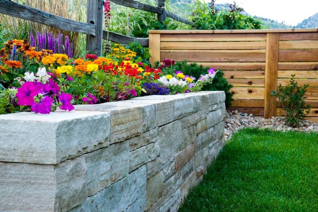 A stone wall with flowers growing on it next to a wooden fence.