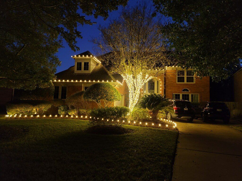 A house is decorated with christmas lights and a tree is lit up at night.