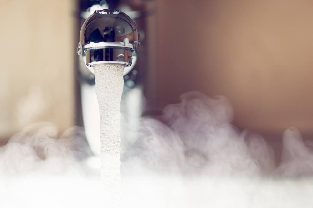 A close up of a faucet with steam coming out of it.