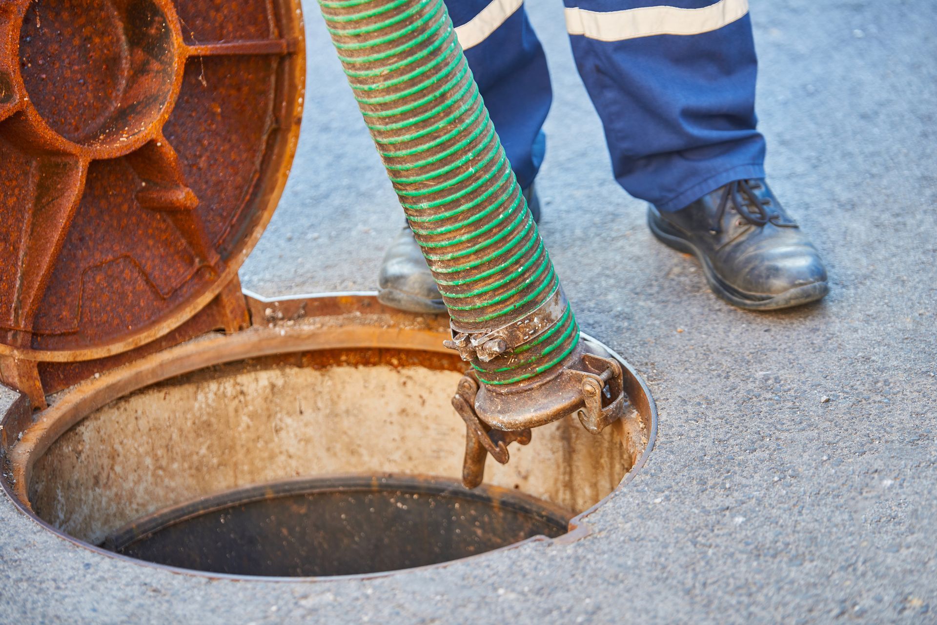 A worker in safety gear is performing sewer cleaning with a hose inside an open manhole.