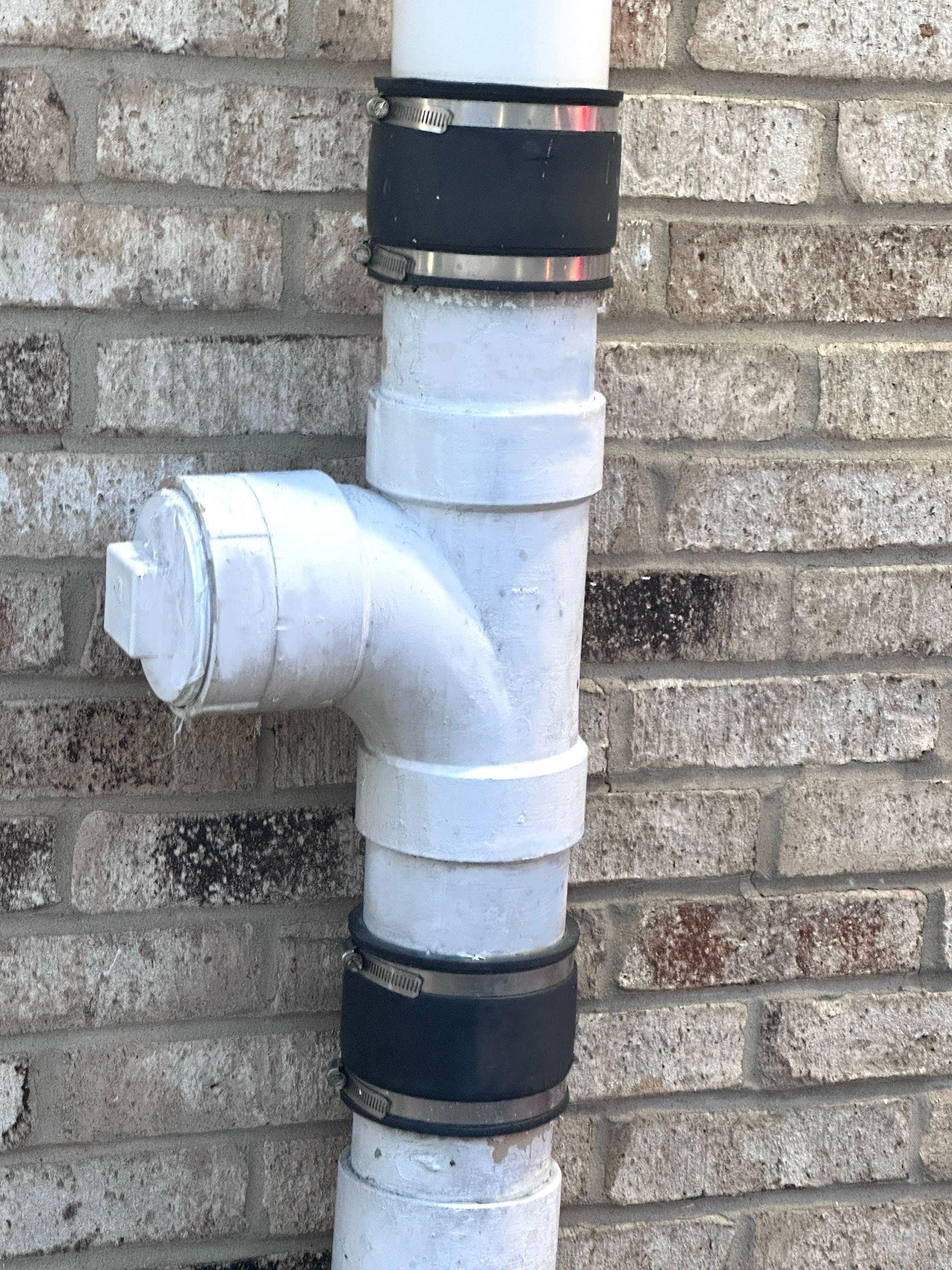 A white pipe is attached to a brick wall.