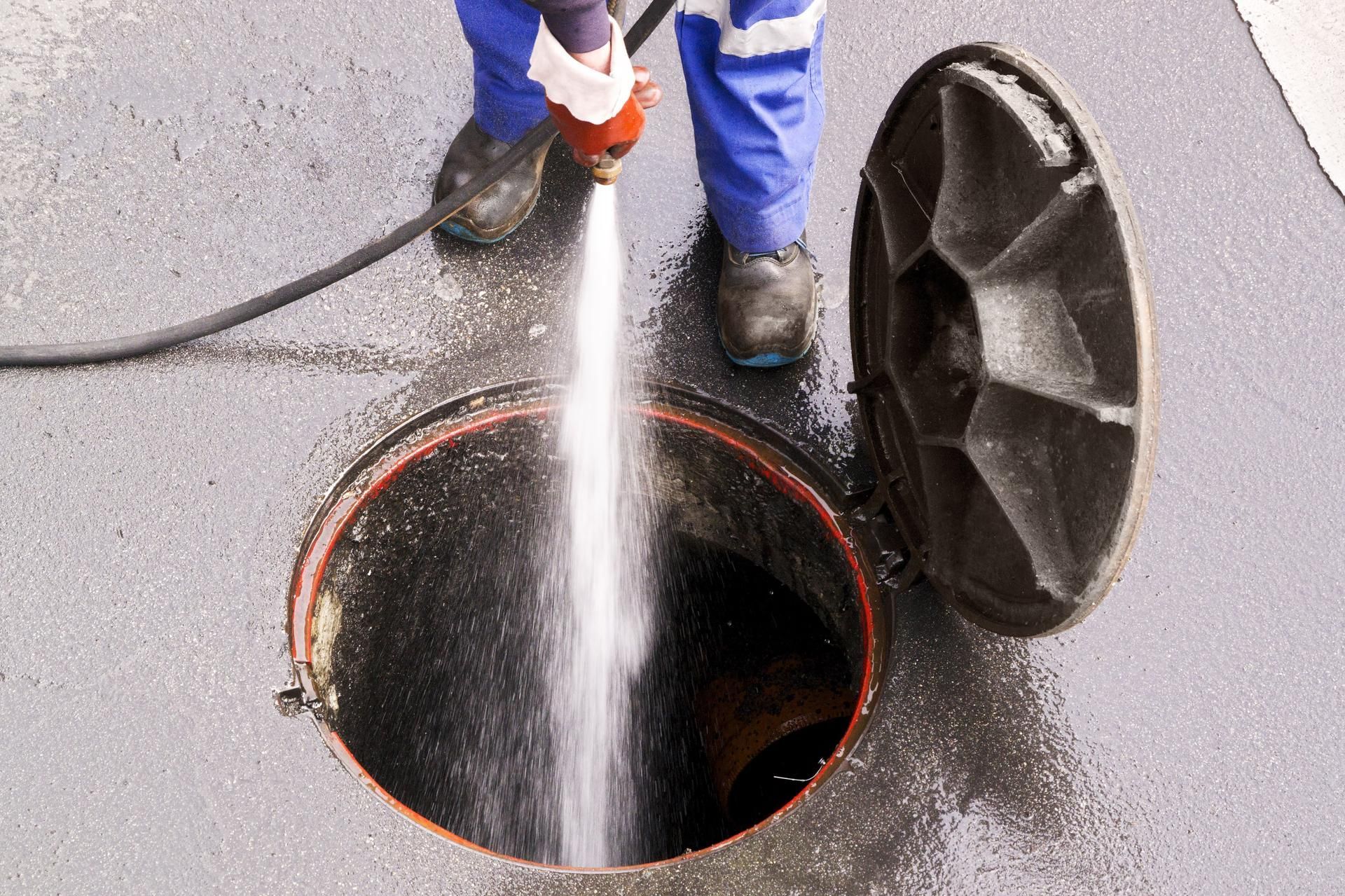 A man is cleaning a manhole cover with a hose.