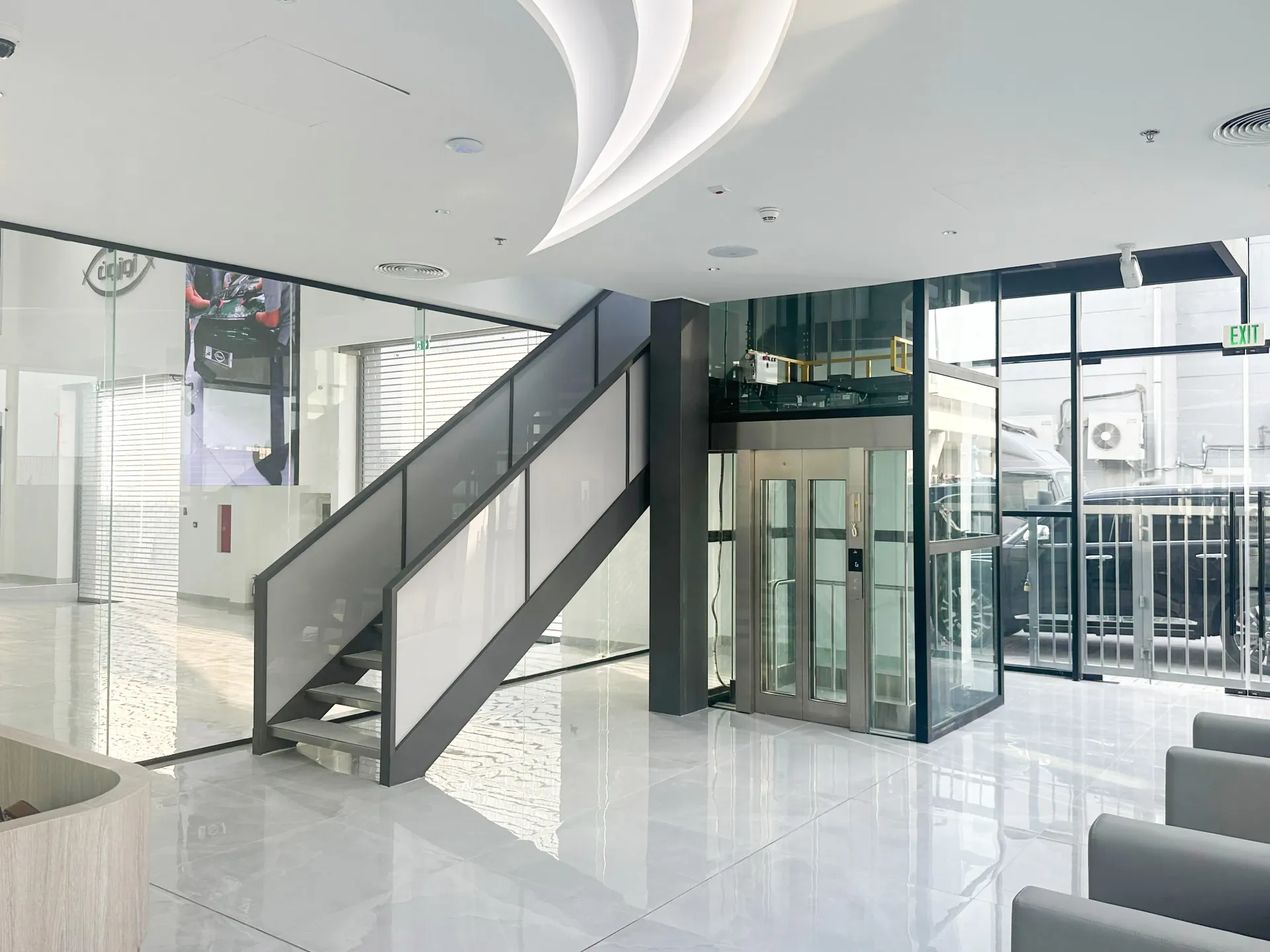 Mezzanine staircase and glass elevator structure in a Dubai luxury showroom fit-out with steel framing by Concept Art Decor