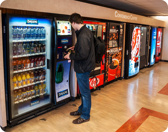 Person using a vending machine in a convenience center; several other machines are visible.