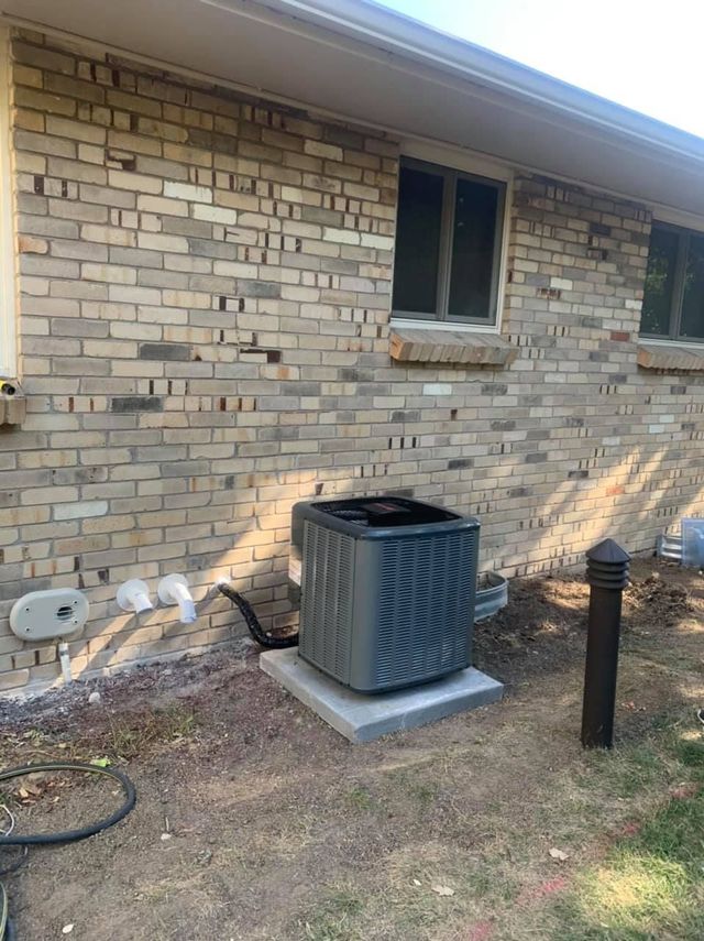 An air conditioner unit sits on a concrete pad near a brick building.