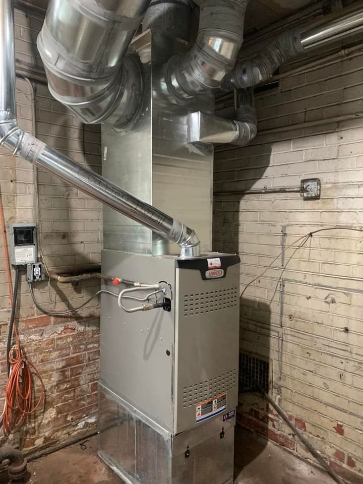 Furnace unit with silver ductwork in a brick-walled basement.