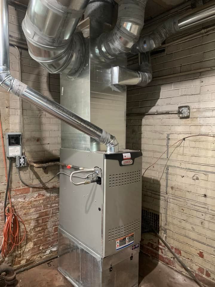 Furnace unit with silver ductwork in a brick-walled basement.
