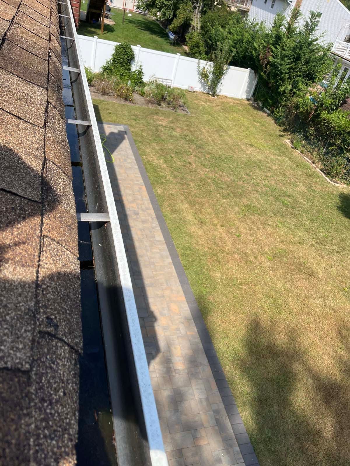 A gutter is sitting on top of a roof next to a grassy yard.
