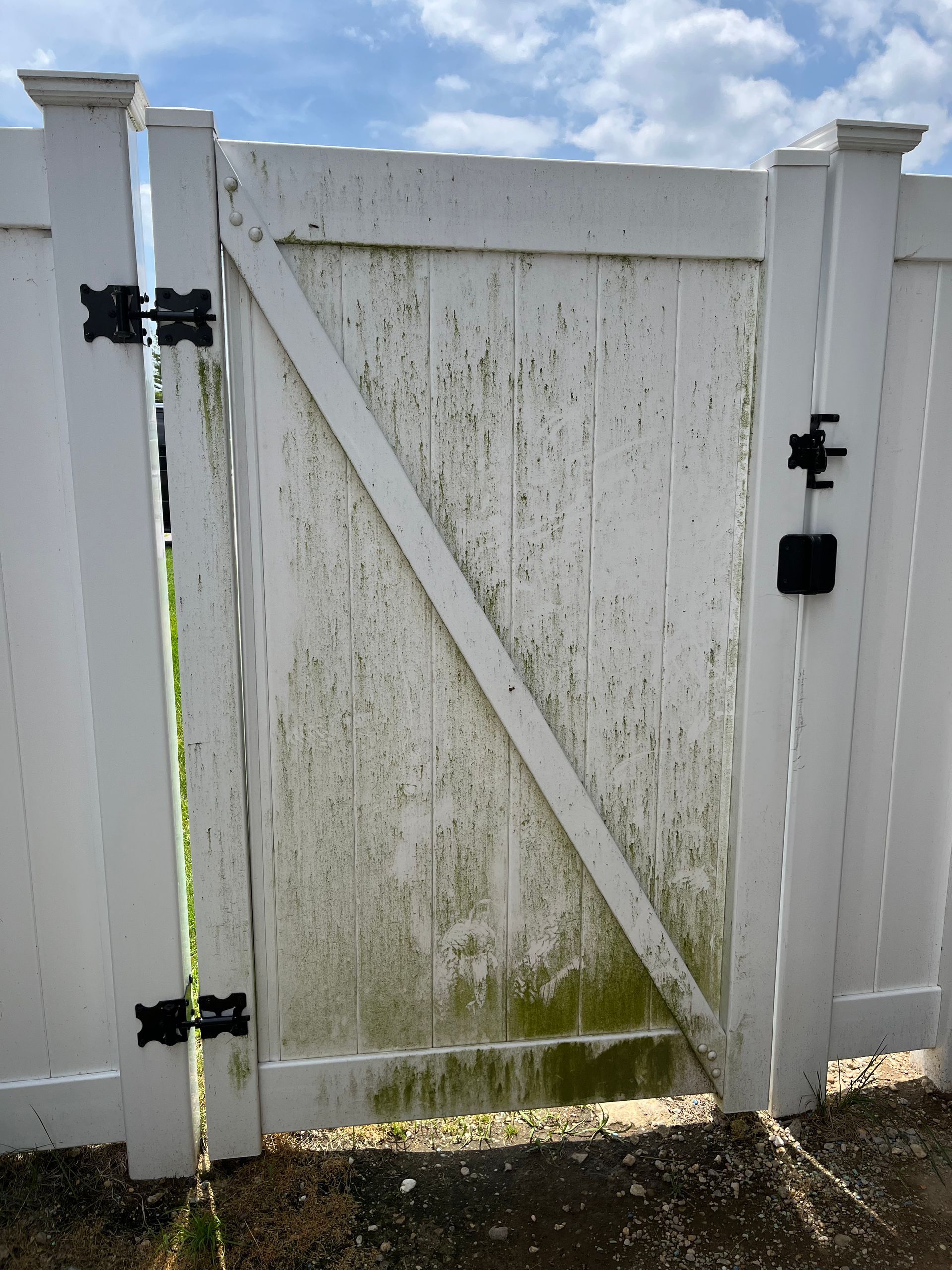 A white fence with a gate that is covered in moss.
