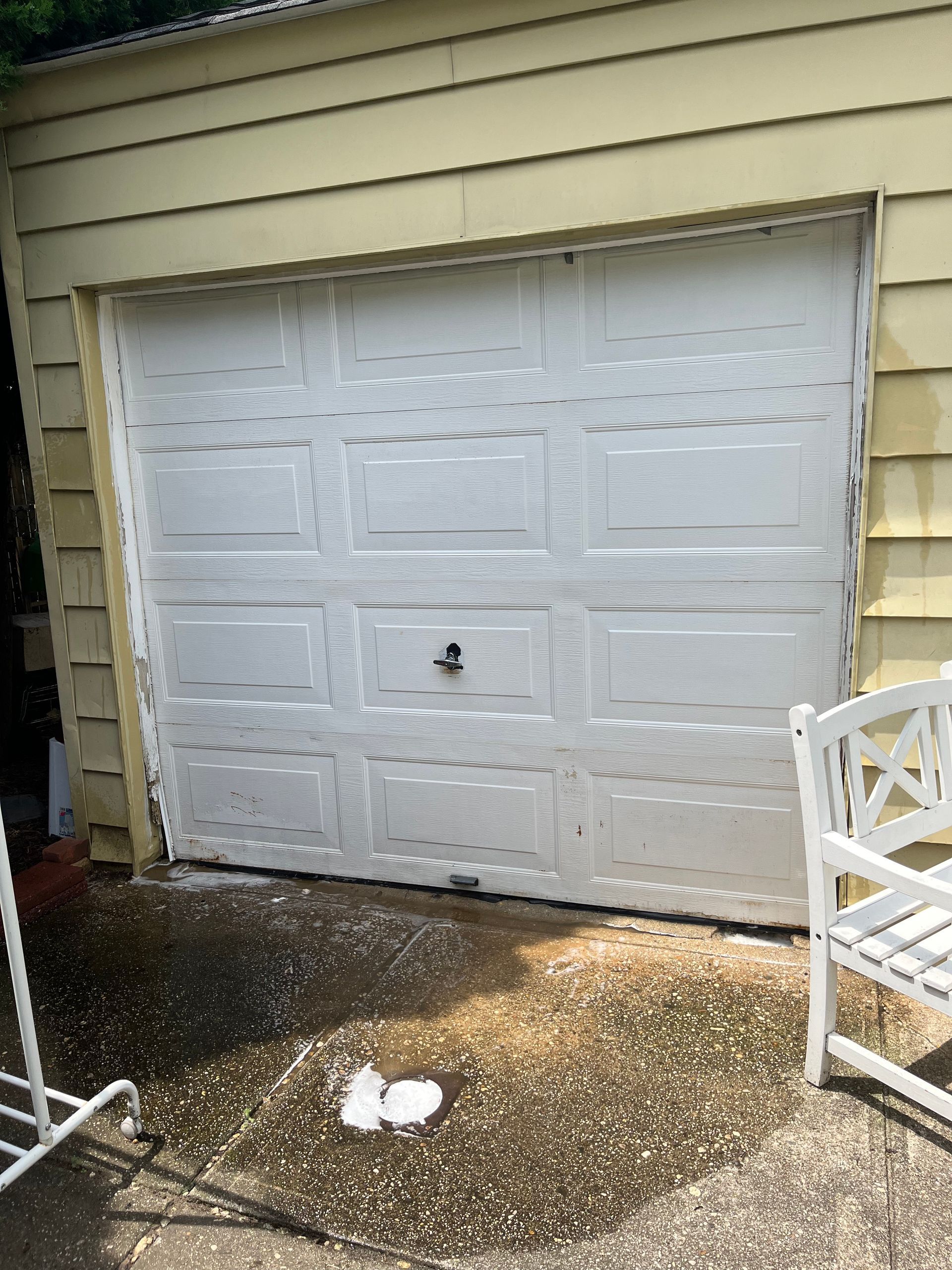 A white garage door is open next to a white chair.
