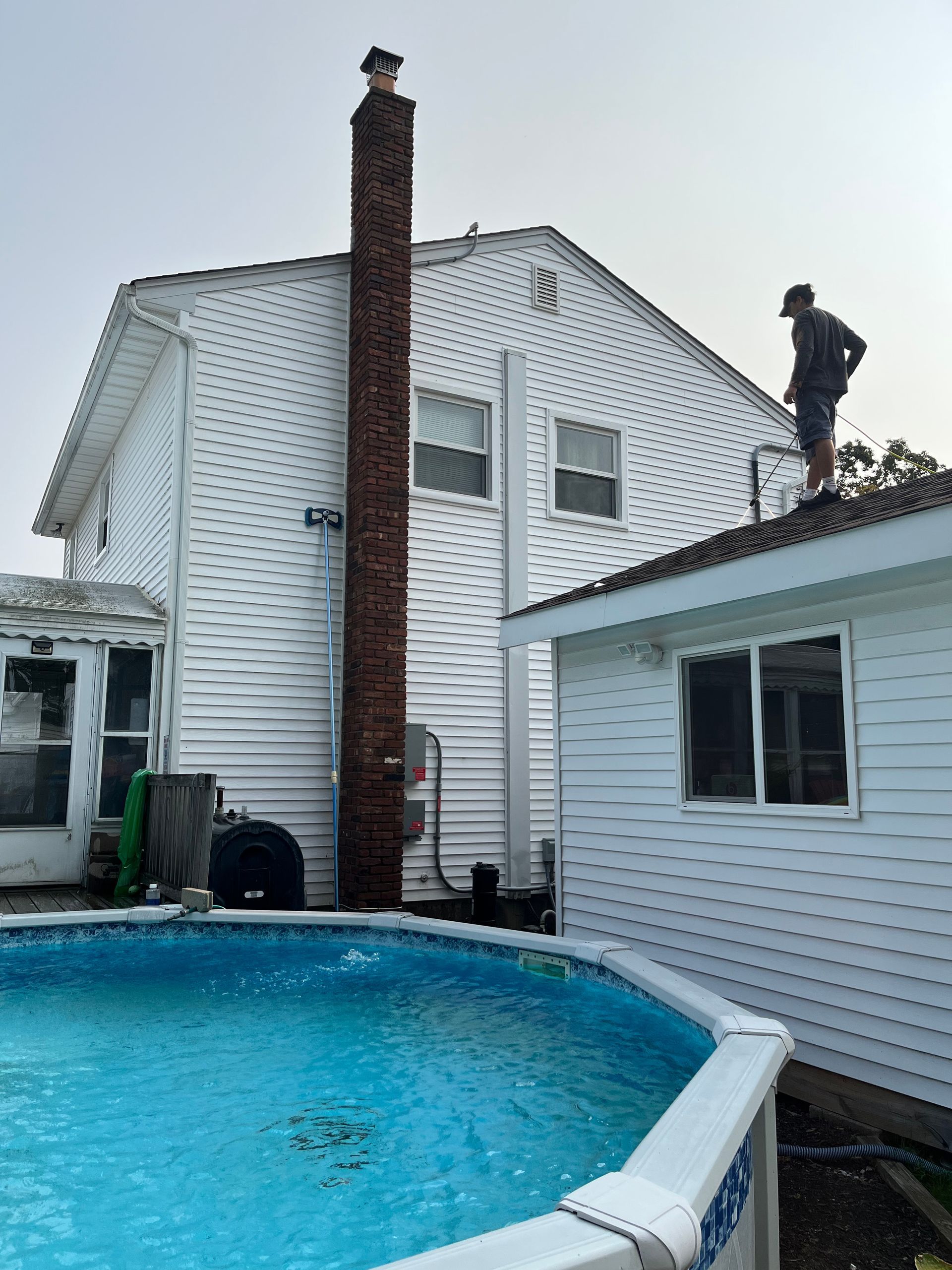 A man is standing on the roof of a house next to a pool.
