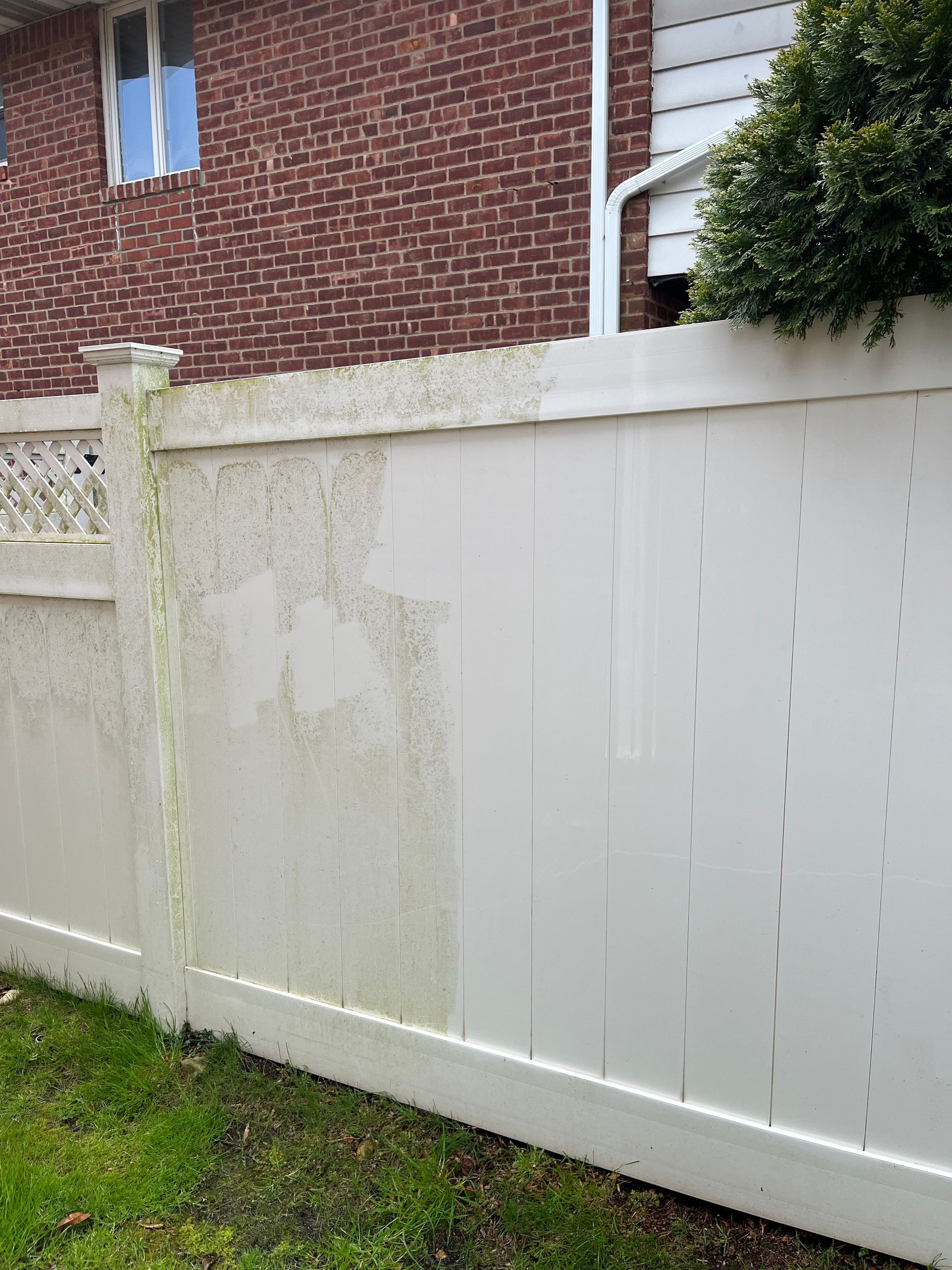 A white fence is sitting in front of a brick house.