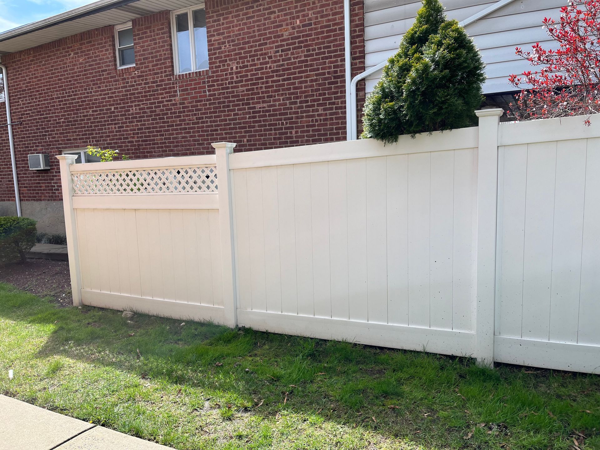 A white fence is in front of a brick house.