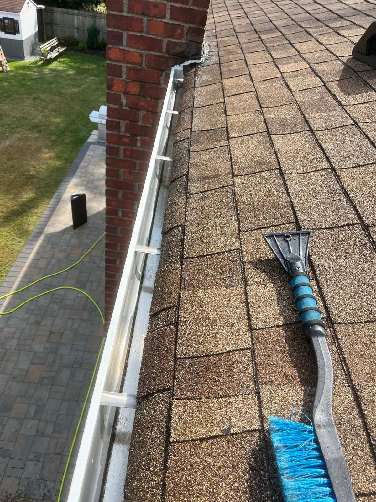 A snow broom and brush are sitting on a roof next to a gutter.