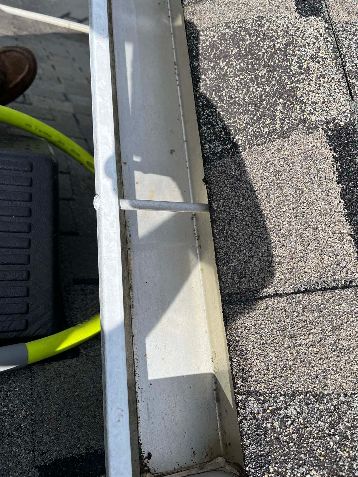 A close up of a gutter on a roof with a yellow hose attached to it.